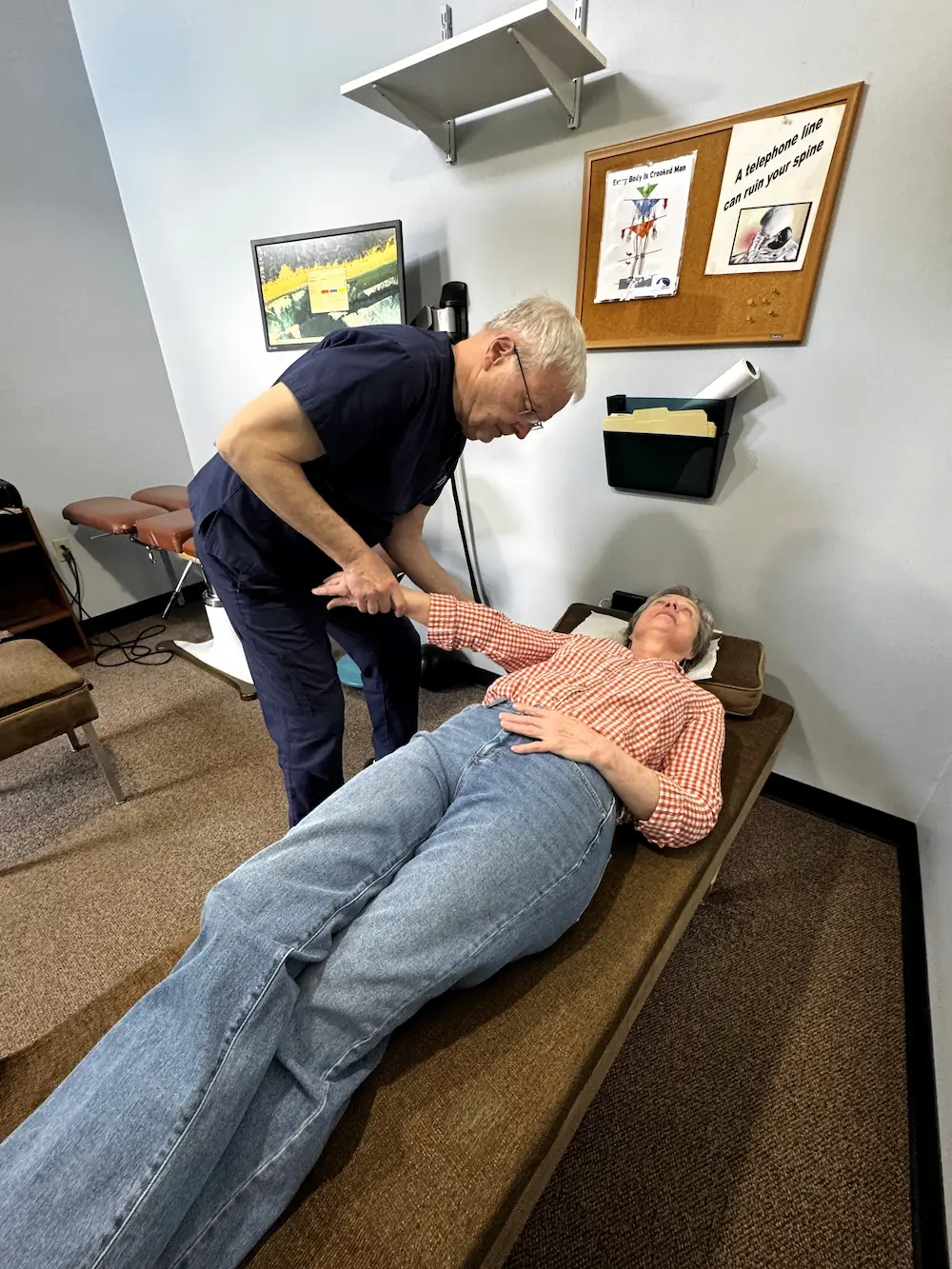 A male chiropractor adjusts the arm of a female patient lying on a chiropractic table.