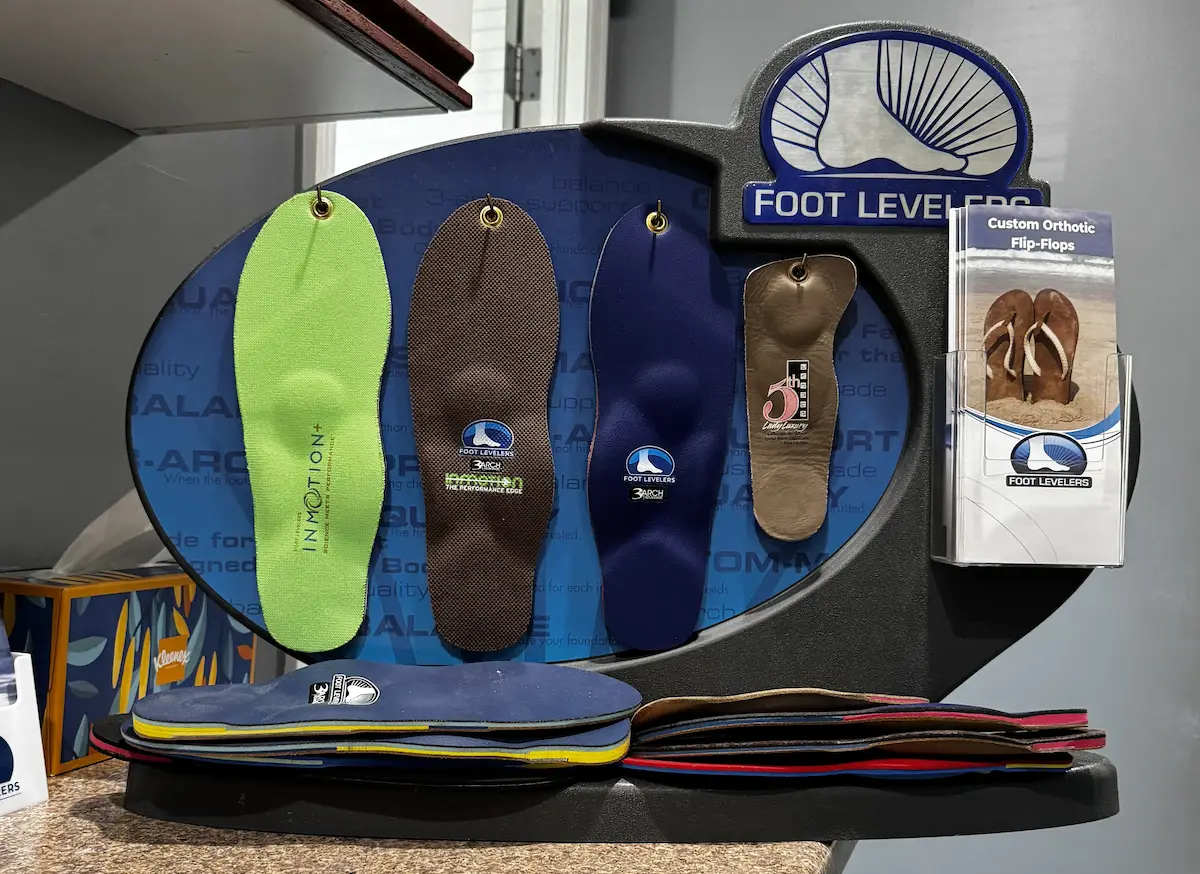 A Foot Levelers display stand showing various colorful orthotic insoles hanging and stacked, with brochures for custom orthotic flip-flops.