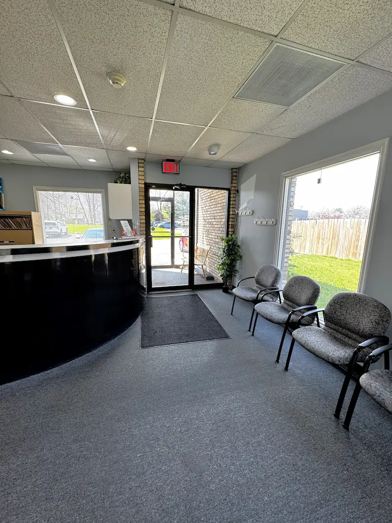 A clean and modern reception area with a black desk, grey waiting chairs, and large windows.
