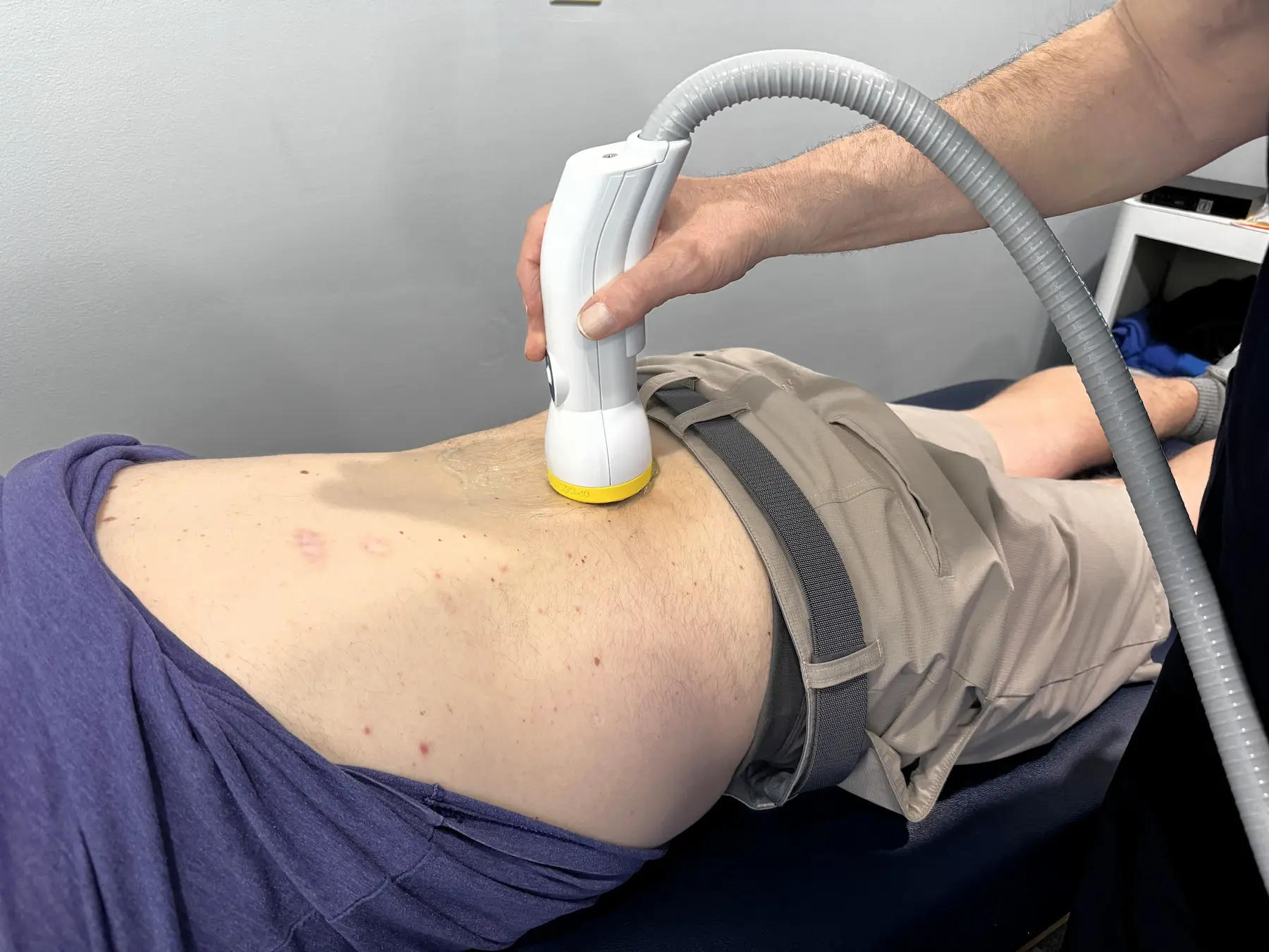 A medical device being applied to a person's lower back/hip area by a professional's hand.