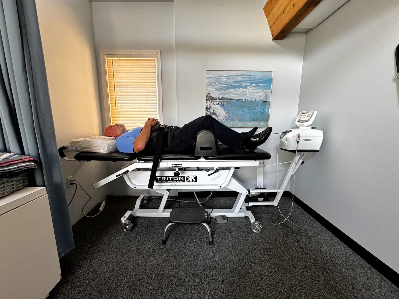 A man lies on a medical treatment table with straps around his torso and hips, undergoing therapy.