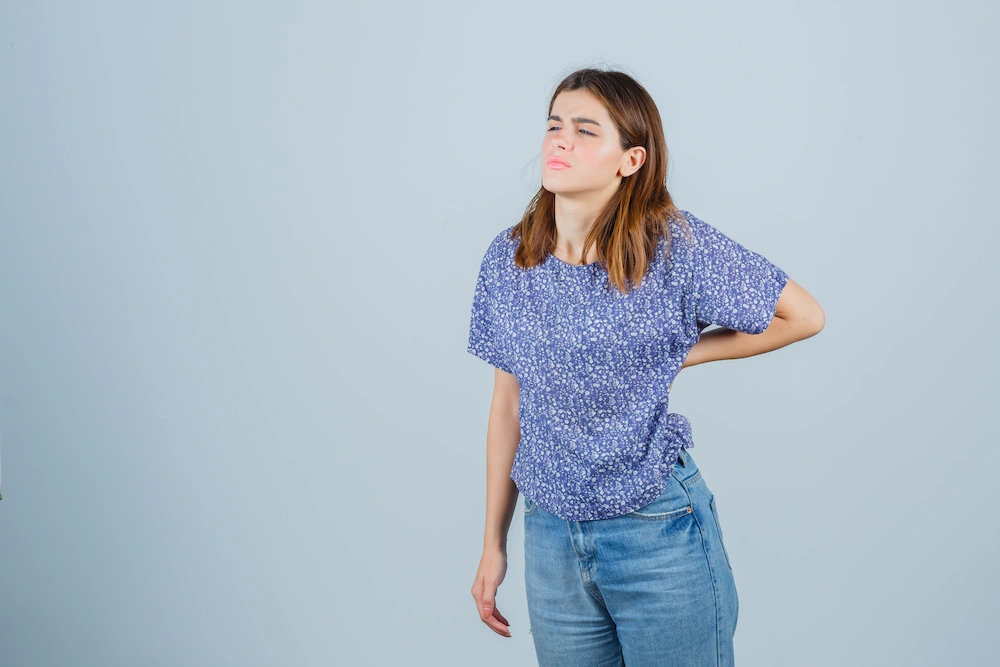 Person holding lower back while standing with focus on feet and posture